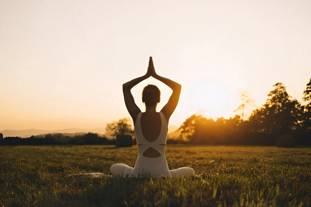 a woman sitting in a grass field with her hands over her head - Stress Relief Therapies